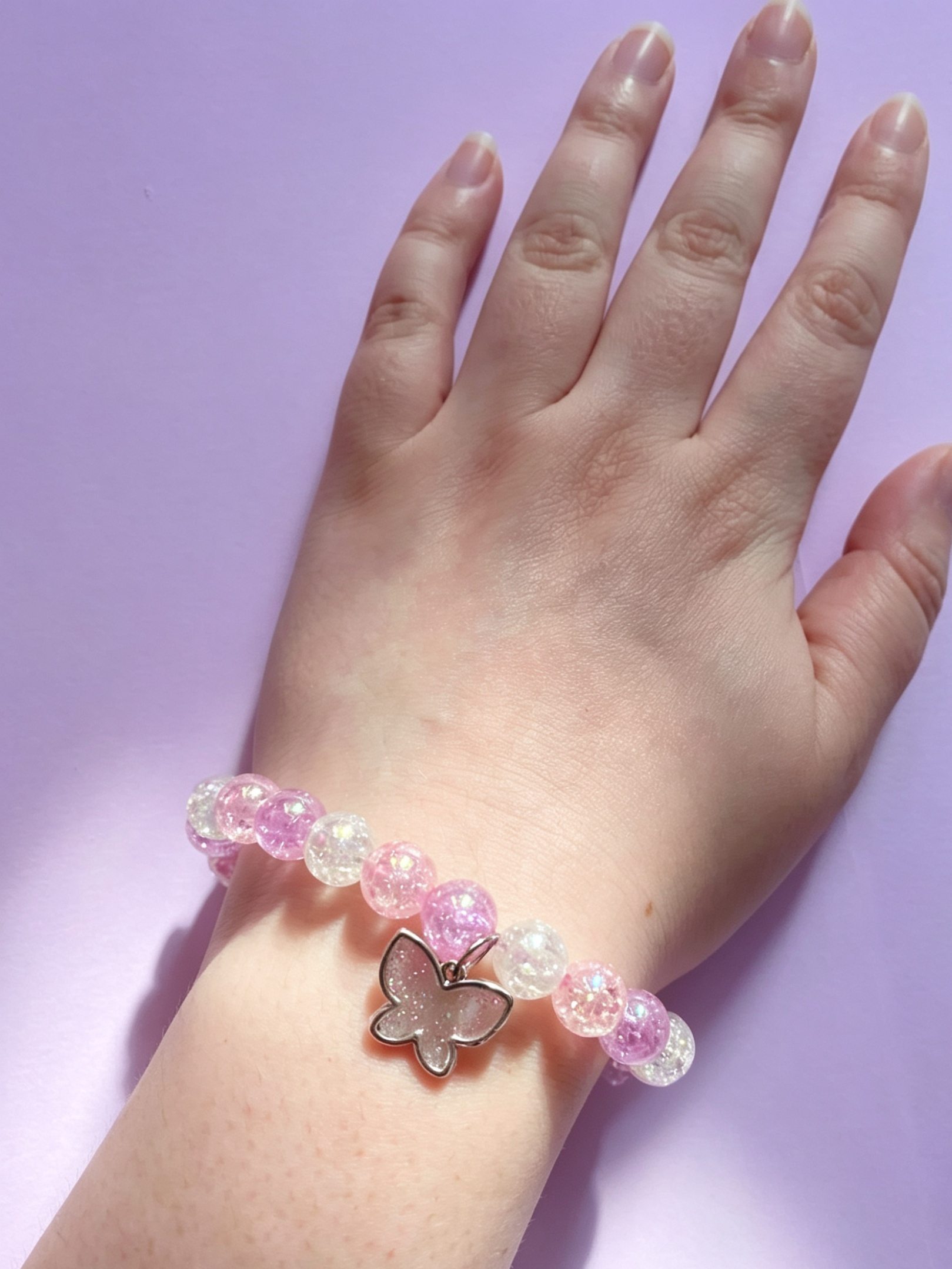 A pink purple and white beaded bracelet with a sparkly butterfly charm 