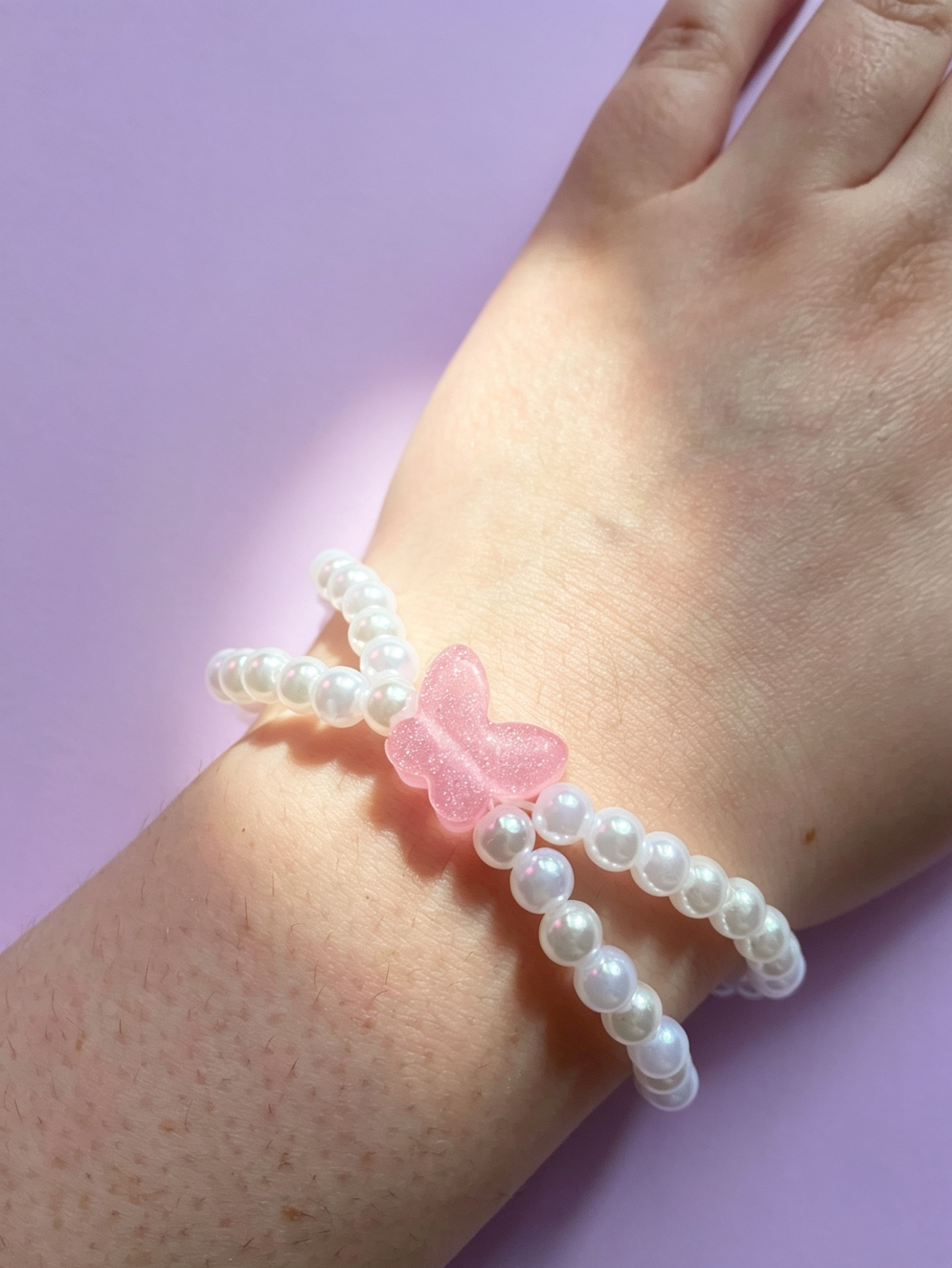 Pearl bracelet with a pink butterfly charm on a wrist against a light purple background
