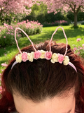 a pink headband decorated with small pink and cream fabric roses and two upright bunny ear loops.