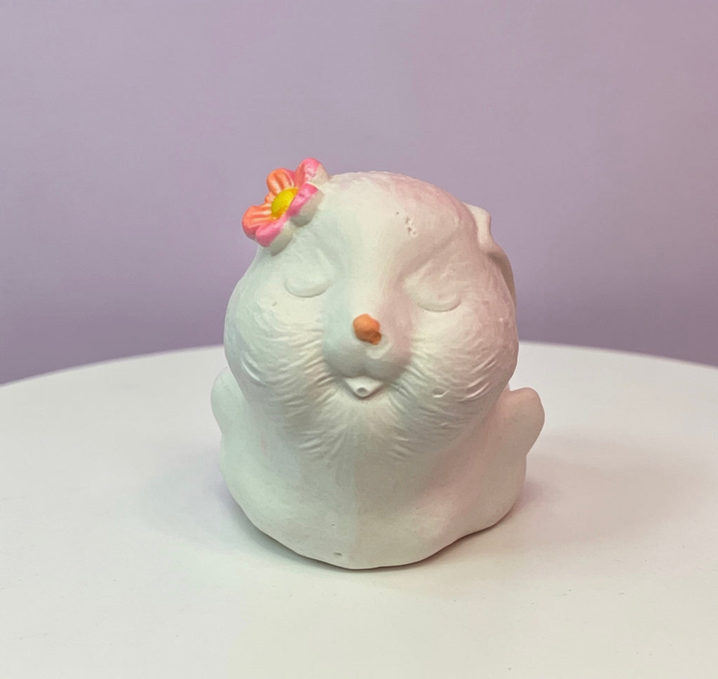 White ceramic bunny figurine with a pink flower behind its ear with a sleepy expression 
