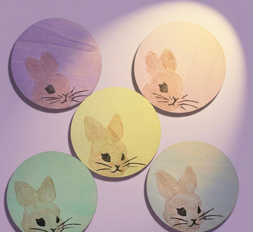 Five circular wooden coasters with rabbit illustrations on a light purple background
