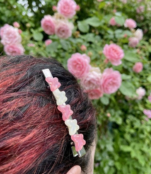 Person wearing a butterfly hair clip  with pink and white butterflies in front of a pink flower bush.